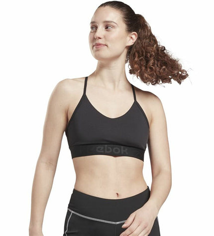 Reebok black strappy sports bra designed for cycling and outdoor activities, shown on a model in a workout setting.