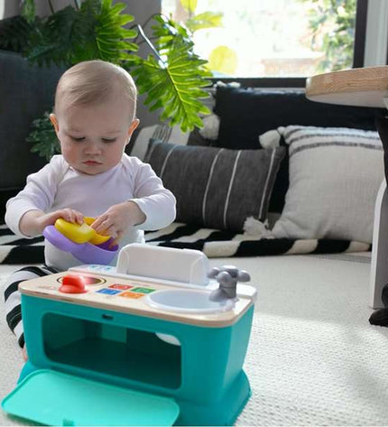 Hape speelgoedkeuken set with colorful plastic utensils, pots, and pretend food for imaginative play in a children's playroom.