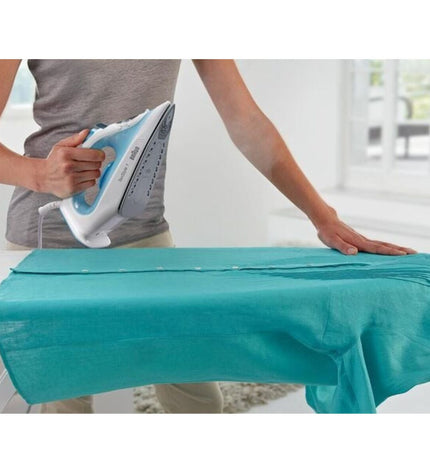 Braun TexStyle 1 blue and white steam iron with 2000W power, shown with cord and water tank in a home ironing setting.