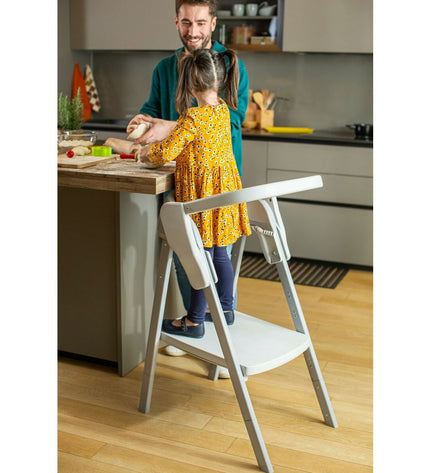 Child's Chicco baby chair with soft fabric upholstery and wooden legs, designed for a cozy nursery or bedroom setting.