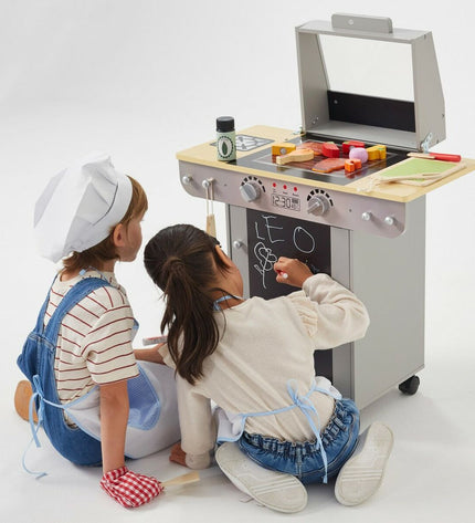 Teamson toy play kitchen BBQ set with stove, countertop, and accessories in a colorful pretend kitchen scene.