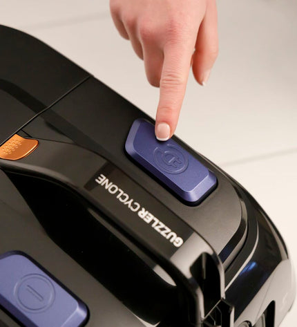 Taurus Guzzler Cyclone steel vacuum cleaner with 850W motor, shown in a home cleaning setting, featuring a large dust container and hose