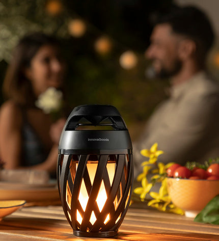 InnovaGoods draadloze speakerphone with LED-vlameffect, outdoor garden decor, portable speaker with colorful flame lighting in a garden setting.
