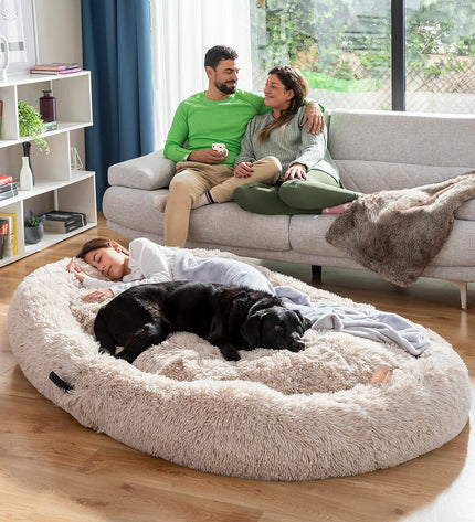 Large beige human dog bed by InnovaGoods, plush cushioned furniture for comfortable lounging, designed to resemble a dog bed.