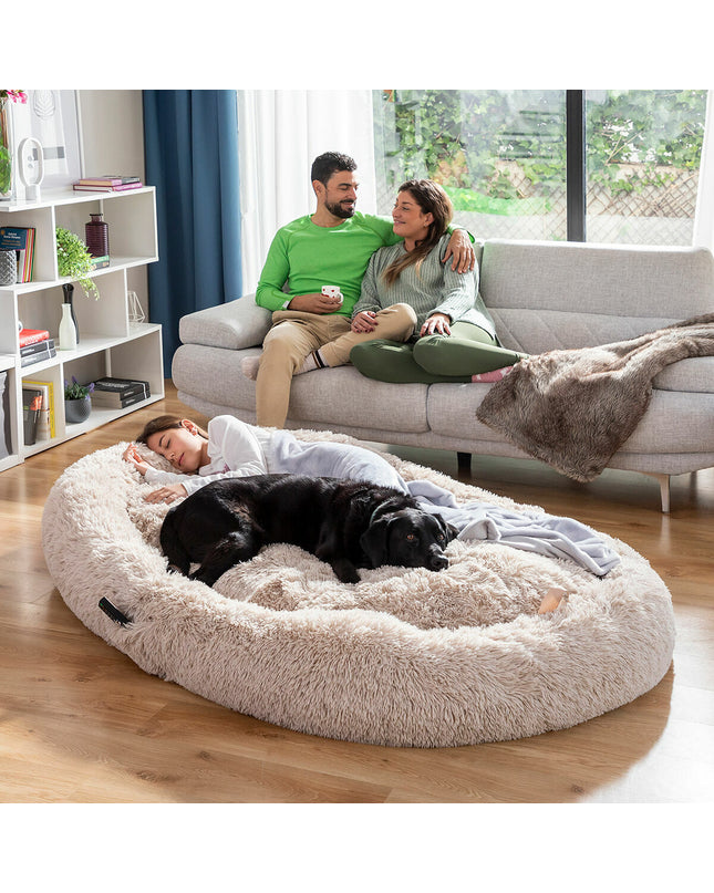 Large beige human dog bed by InnovaGoods, plush cushioned furniture for comfortable lounging, designed to resemble a dog bed.