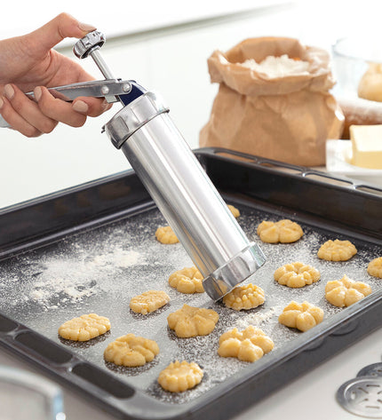 InnovaGoods 2-in-1 cookie press and decorating syringe for baking, with stainless steel tips and ergonomic handle, on a kitchen countertop.