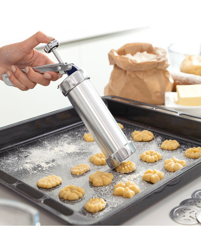 InnovaGoods 2-in-1 cookie press and decorating syringe for baking, with stainless steel tips and ergonomic handle, on a kitchen countertop.